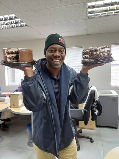 A DLS staff member in a DLS cap holding two cakes in an office.